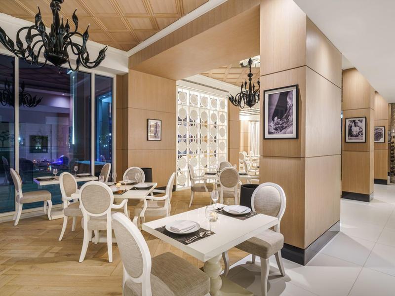 Restaurant élégant avec chaises blanches, grandes fenêtres et lustres.