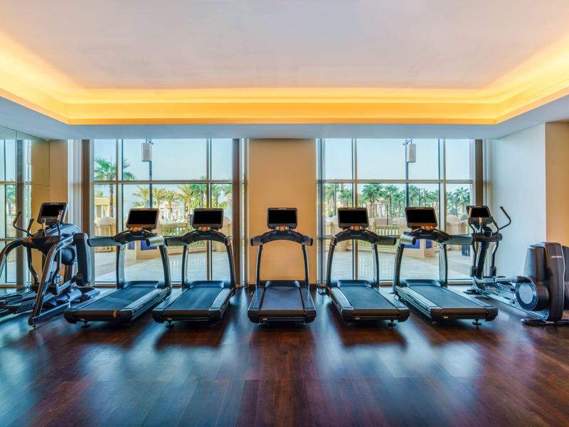 Salle de sport moderne avec plusieurs tapis roulants et grandes fenêtres offrant une vue sur la ville.