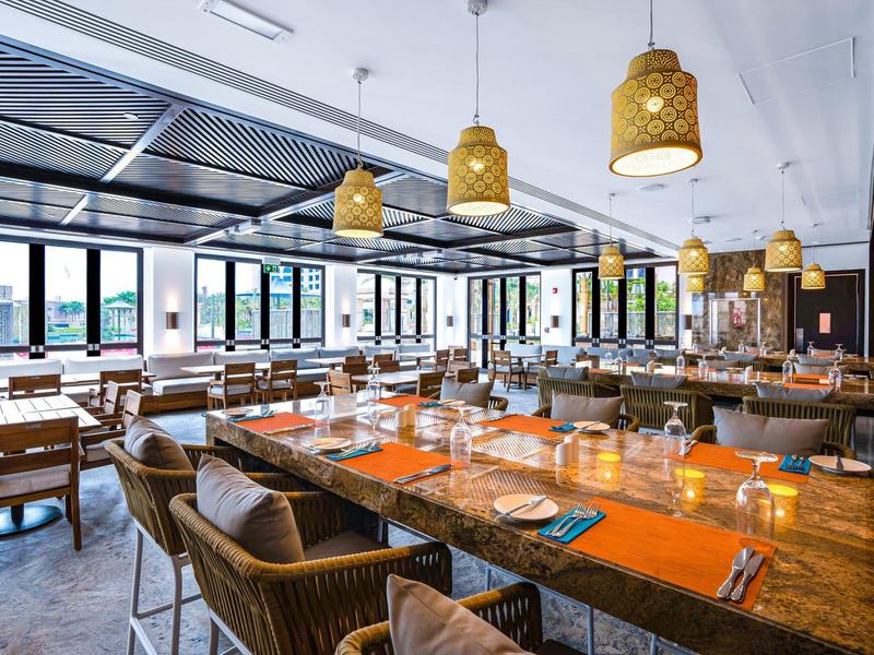Espace de restaurant d'hôtel moderne avec tables en bois, chaises en osier et grandes fenêtres avec vue.