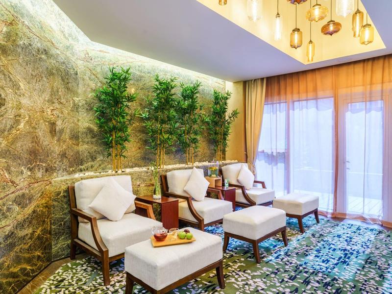 Espace d'attente confortable avec fauteuils, repose-pieds et plantes devant une fenêtre avec rideaux