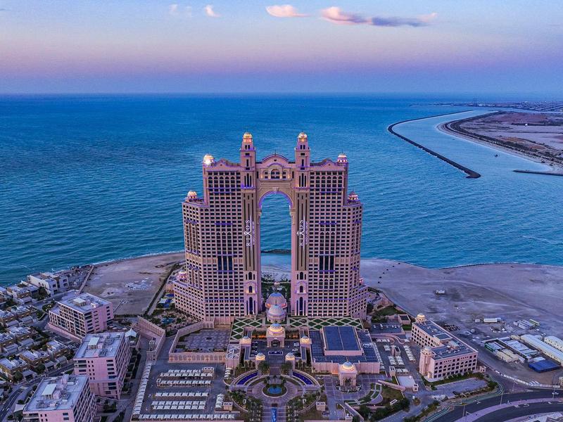 Complexe hôtelier de luxe avec deux tours au bord de la mer, plage étendue et ville environnante.