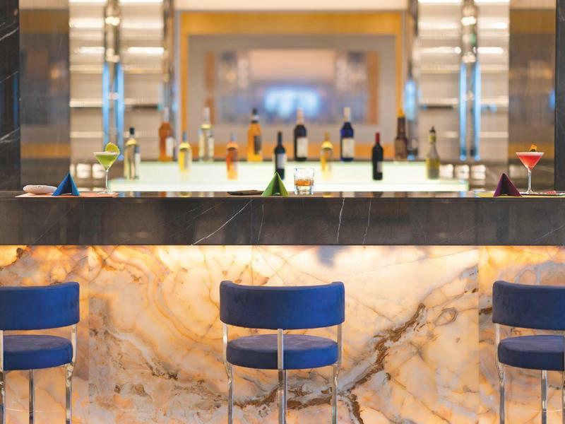 Espace bar avec tabourets bleus et une sélection de bouteilles sur le comptoir.