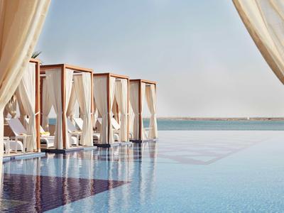 Piscina di lusso con letti a baldacchino bianchi con vista sul mare sotto un cielo limpido.
