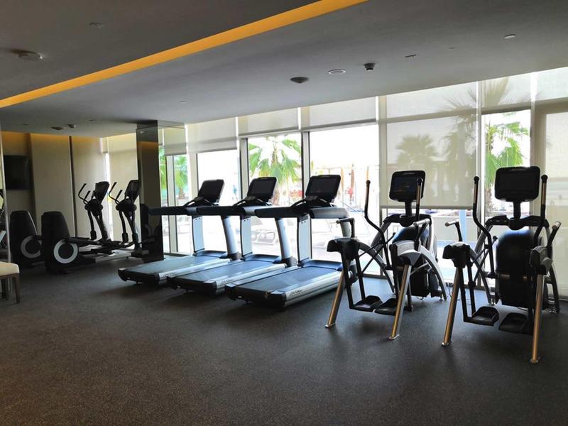 Moderní fitness s běžeckými pásy a eliptickými trenažéry u velkých oken.