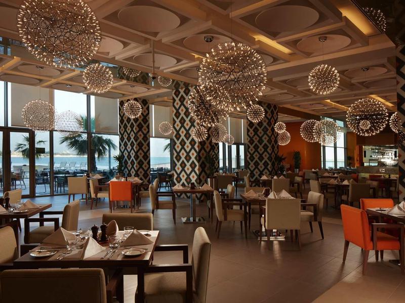 Elegantní restaurace s velkými závěsnými koulemi a panoramatickými okny s výhledem na moře.