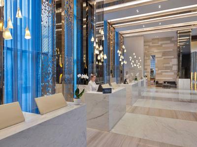 Moderner Hotellobby mit hellen Marmorflächen, blauen Vorhängen und eleganten Pendelleuchten.