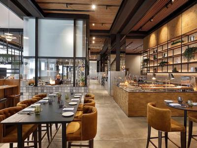 Modernes Restaurant mit Holzstühlen, großen Tischen und Regalen an den Wänden, warme Beleuchtung.