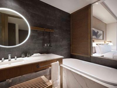 Modernes Badezimmer mit beleuchtetem Spiegel, Holzmöbeln und freistehender Badewanne.