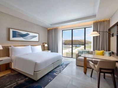 Modernes Hotelzimmer mit großem Bett, Schreibtisch, Sessel und großer Fensterfront mit Bergblick.