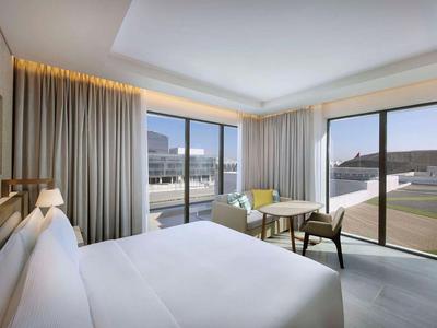 Světý hotelový pokoj s velkou postelí, posezením a velkými okny s výhledem na město.