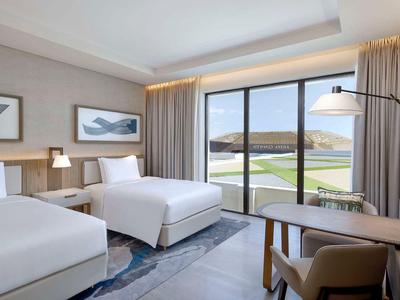 Modernes Hotelzimmer mit zwei Einzelbetten, großem Fenster und Blick auf Wasser und Hügel.