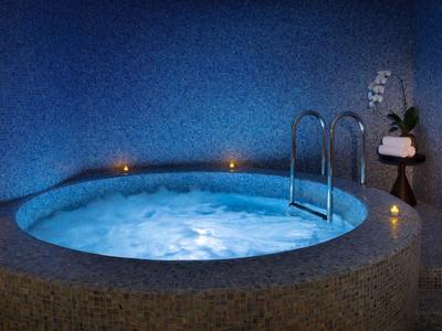Runder Whirlpool mit blauem Wasser, umgeben von Kerzen und blauer Wand im Hintergrund.