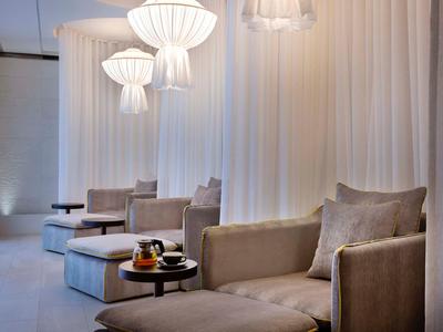 Moderne Lounge mit grauen Sesseln, runden Tischen und weißen, stilvollen Hängelampen vor weißem Vorhang.