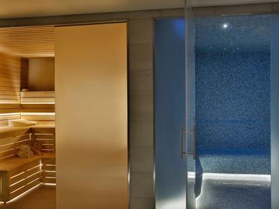 Moderne Sauna mit Holzinterieur links und blauer Mosaik-Spa-Bereich rechts, getrennt durch Glaswand.