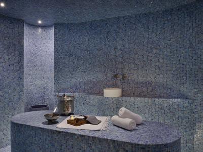 Ein modernes Dampfbad mit blauen Mosaikfliesen, einer Sitzbank und Handtüchern auf einem Tisch.
