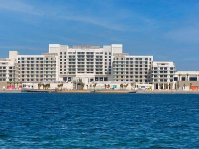 Großes weißes Hotelgebäude am Meer mit blauem Himmel und Wasser im Vordergrund.