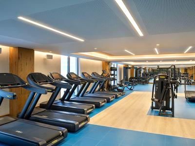 Moderner Fitnessraum mit Laufbändern, Kraftgeräten und großen Fenstern, helle Beleuchtung.