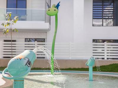 Wasserspielplatz mit grünem, drachenförmigem Springbrunnen und zwei blauen Wasserdüsen.