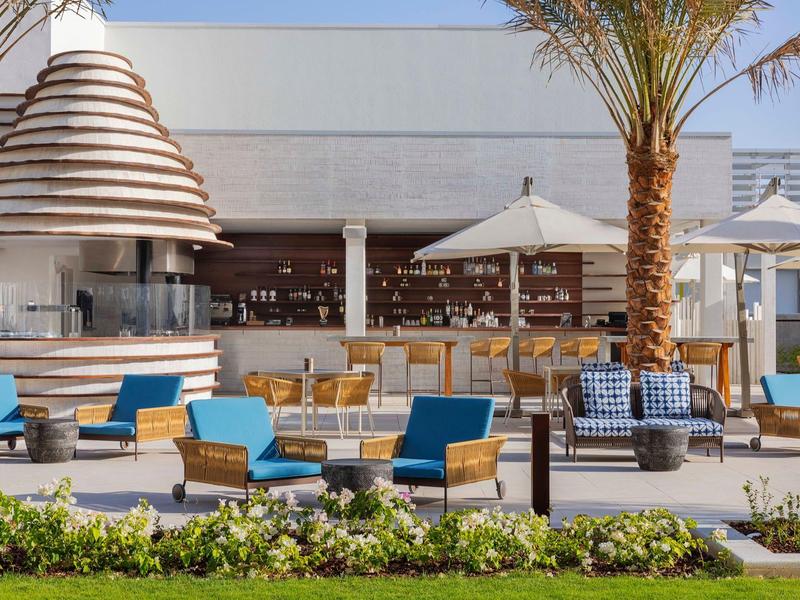 Modern outdoor area with blue chairs, umbrellas, and an open-air bar.