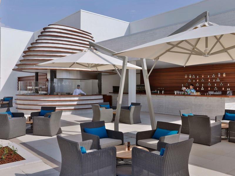 Modern outdoor area with bar, seating, and umbrellas next to a hotel.