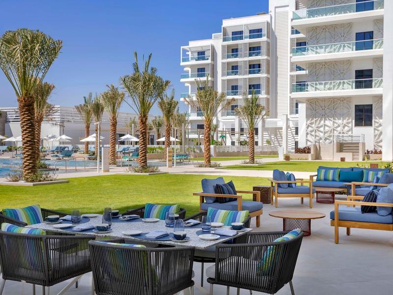 Modern outdoor hotel area with seating and palm trees by the pool.