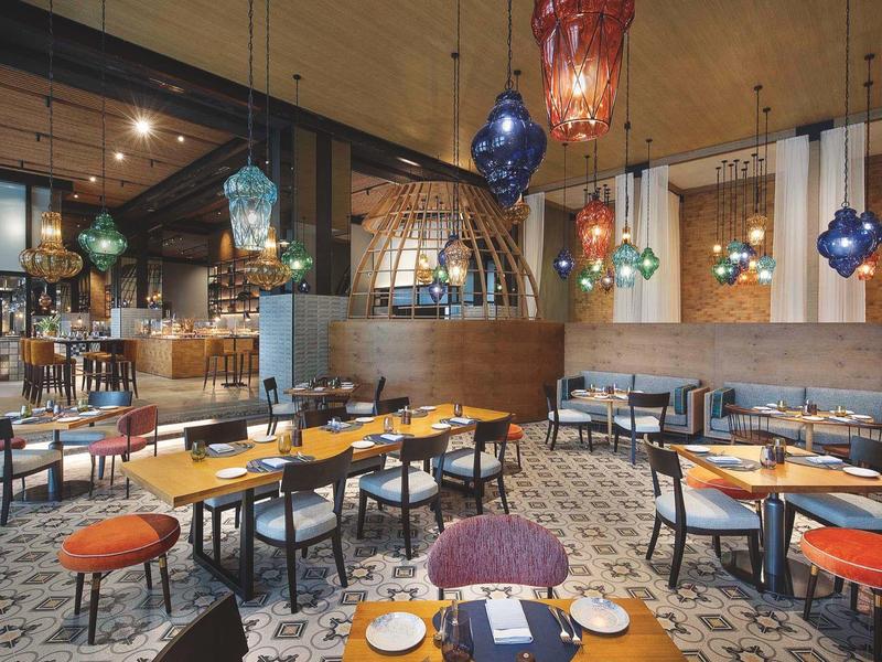A modern hotel restaurant with colorful lamps, wooden tables, and striped chairs.