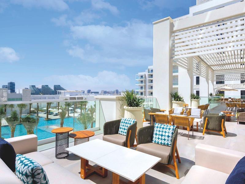Modern terrace with seating area overlooking pool and city under clear sky.