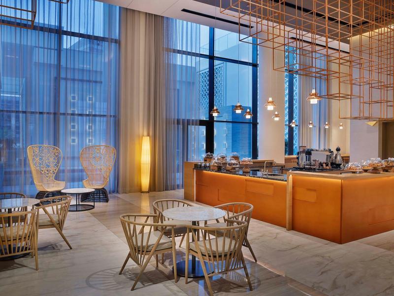 Modern hotel restaurant with tall windows, leather bench seating, and round wooden table.