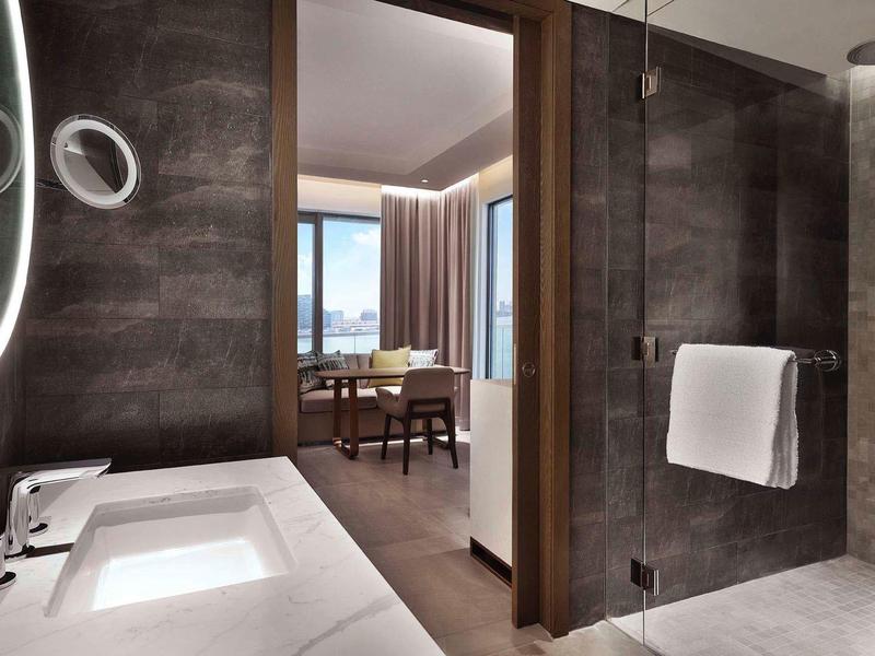Modern hotel bathroom with large mirror, sink, and a view into the room.
