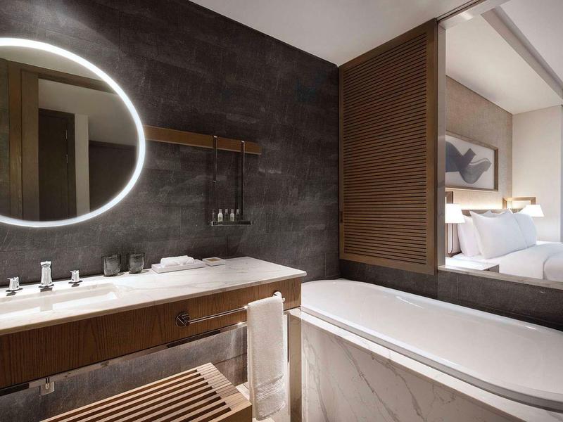 Modern hotel bathroom with round mirror, sink, and freestanding bathtub in warm tones.