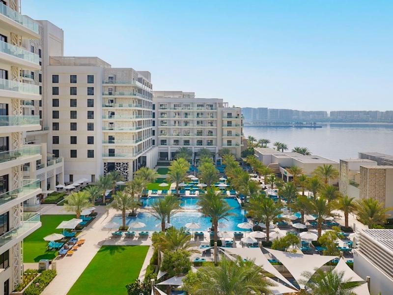 Hotel complex with multiple pools, sun loungers, and a view of the sea.