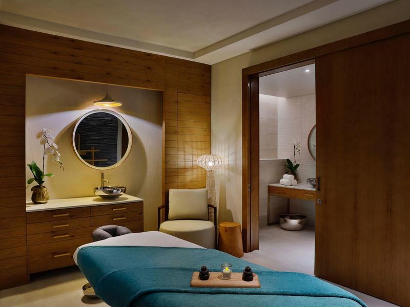 Cozy spa room with massage table, wood paneling, and relaxed lighting.