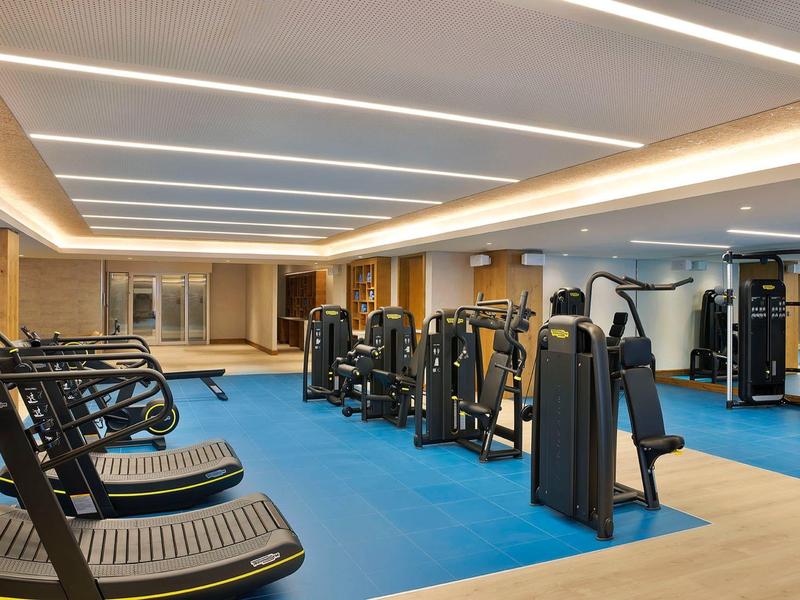 Modern gym with various exercise machines and treadmills on a blue floor.