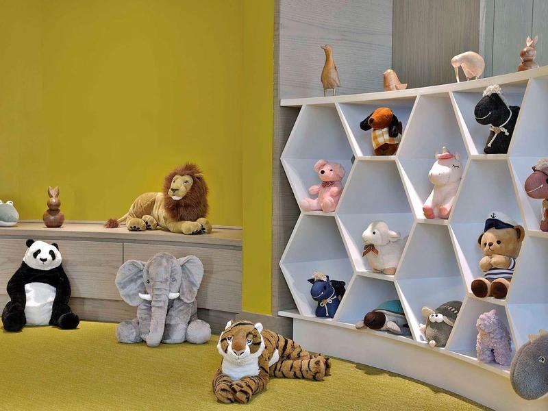 A room with a yellow wall, seating area, and hexagonal shelves filled with stuffed animals.
