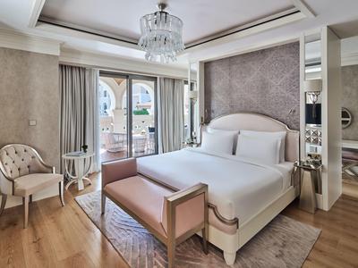 Habitación de hotel luminosa y lujosa con cama grande, candelabro y balcón con vistas al mar.