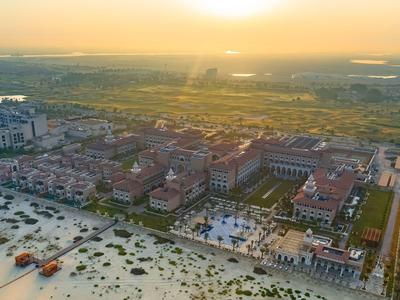 Vista aérea de un resort junto al mar al atardecer con playa de arena y áreas verdes.