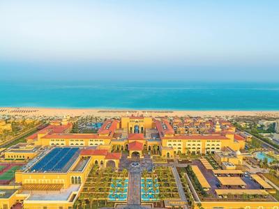 Gran complejo con edificios amarillos, piscinas y vista al mar en el fondo.