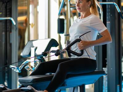 Kobieta ćwiczy na maszynie fitness w nowoczesnej siłowni z naturalnym światłem.