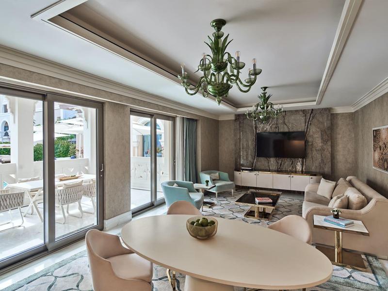 Habitación de hotel luminosa con área de estar cómoda, mesa de comedor y acceso a la terraza con asientos exteriores.