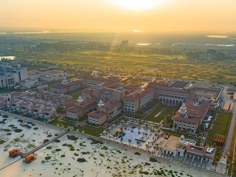 Vista aérea de un resort junto al mar al atardecer con playa de arena y áreas verdes.