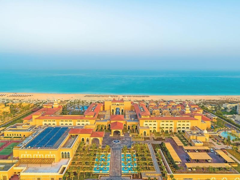Gran complejo con edificios amarillos, piscinas y vista al mar en el fondo.