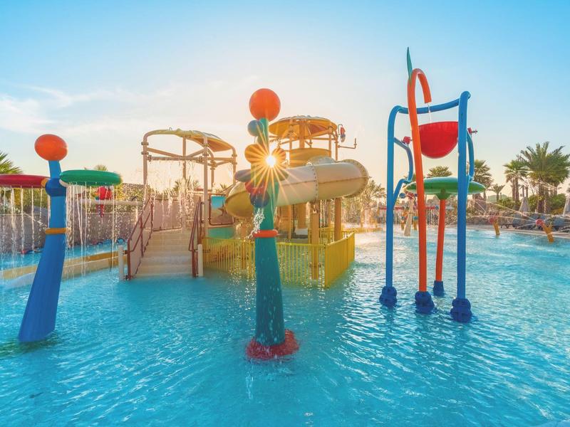 Parque acuático con toboganes coloridos y juegos bajo un cielo soleado y palmeras.