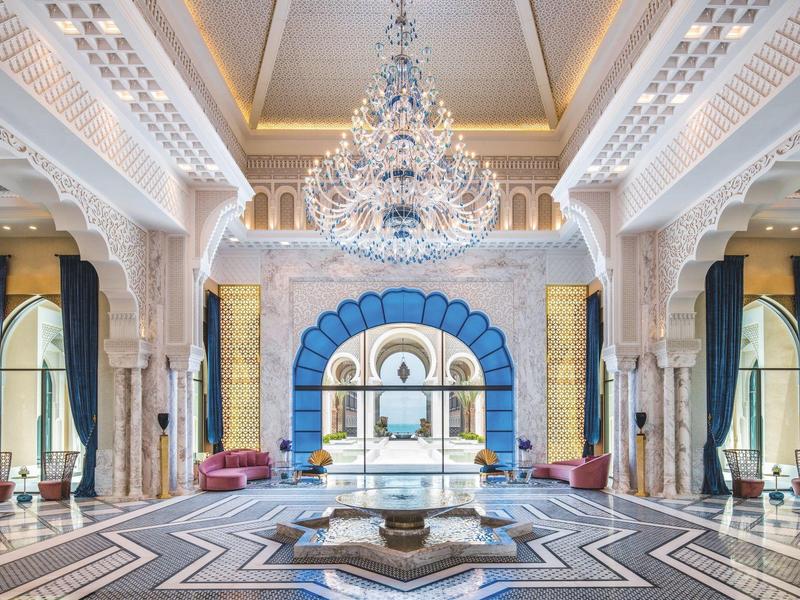 Lujoso vestíbulo de hotel con columnas magníficas, candelabro de cristal y diseño simétrico.