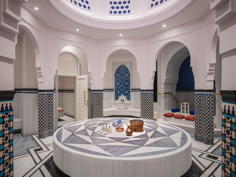 Hamam lujoso con azulejos de mosaico, camilla central redonda y techo artístico.