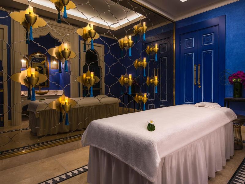 Sala de spa elegante con diseño azul y dorado y una camilla cubierta con sábana blanca.