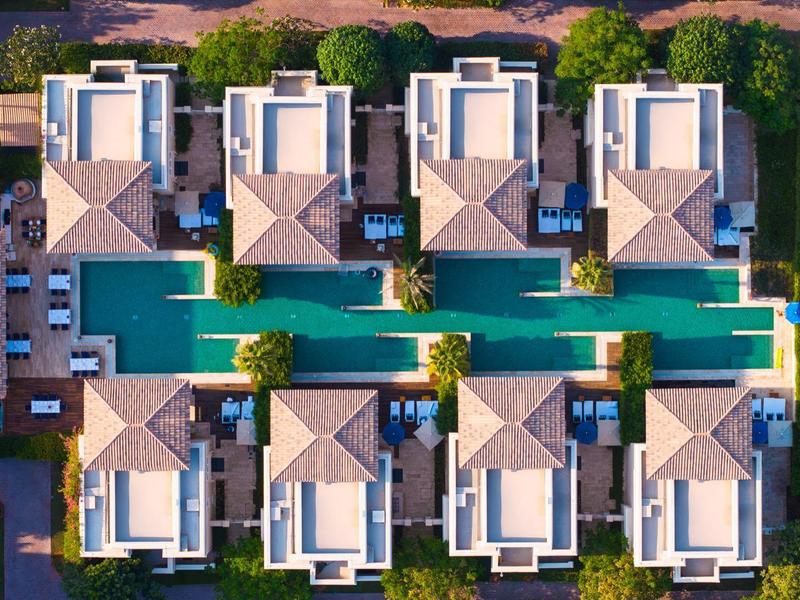 Vista aérea de un hotel moderno con piscina y edificios dispuestos simétricamente.