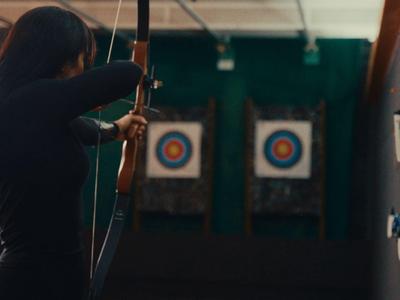 Vrouw richt met pijl en boog in een indoor schietbaan.
