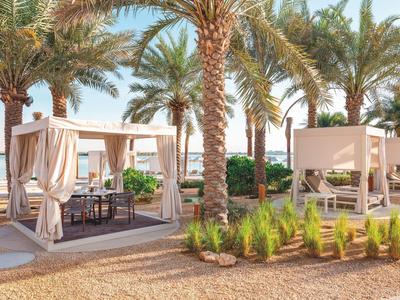 Strand mit Palmen, beigen Zelten und Sitzgelegenheiten bei Sonnenschein und klarem Himmel.