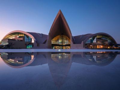 Modern hotel met gebogen dak en weerspiegeling in rustig water bij schemering