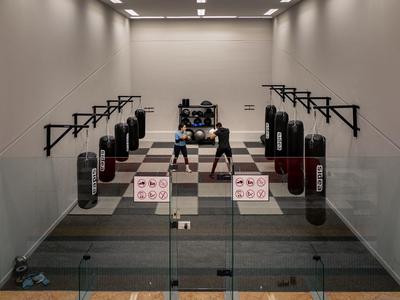 Een moderne fitnessruimte met bokszakken en trainingsmatten achter een glazen wand.